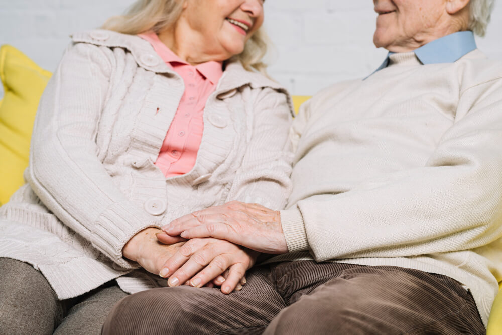 Mains d'un couple de personnes âgées se tenant, symbolisant le soutien mutuel, l'amour et la complicité dans l'accompagnement face à la dépendance